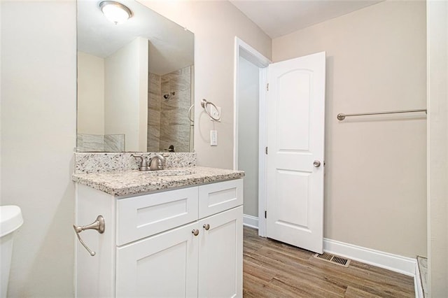 bathroom with vanity, toilet, hardwood / wood-style floors, and a tile shower