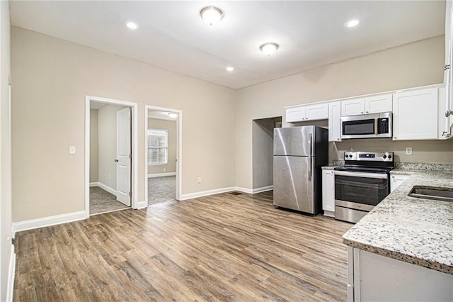 kitchen with stainless steel appliances, white cabinetry, light stone countertops, and light hardwood / wood-style flooring