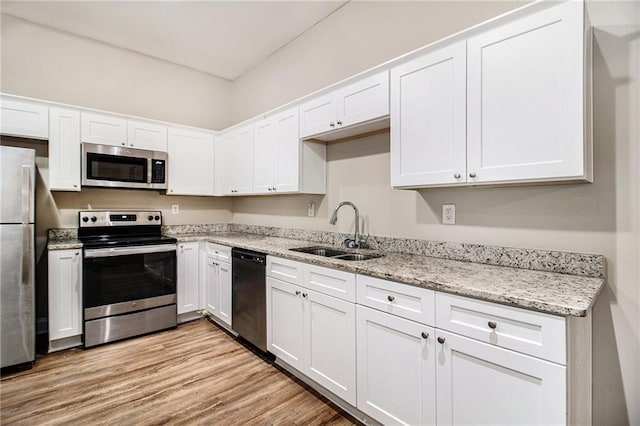 kitchen with stainless steel appliances, white cabinetry, sink, and light wood-type flooring