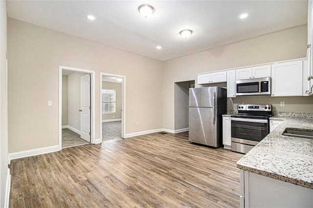 kitchen with light stone countertops, light hardwood / wood-style floors, white cabinets, and appliances with stainless steel finishes