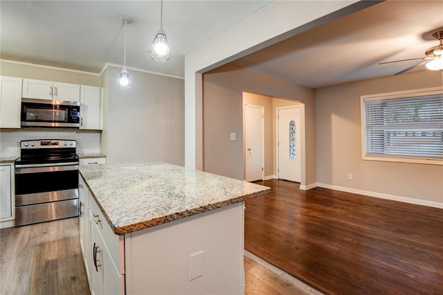 kitchen with light stone countertops, stainless steel appliances, a center island, white cabinetry, and hanging light fixtures