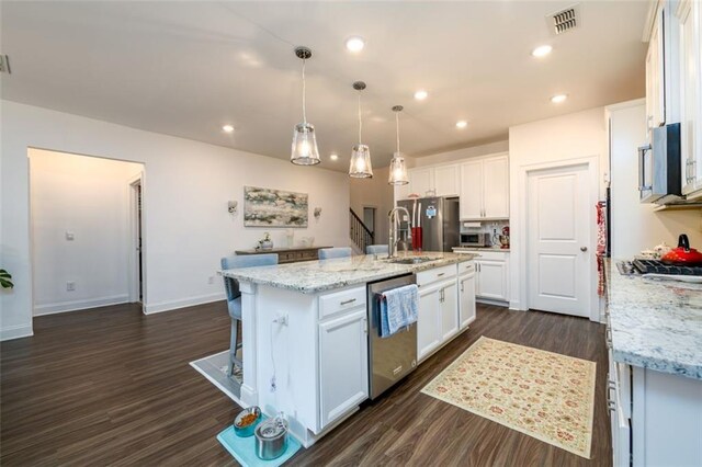 kitchen with a center island with sink, white cabinets, light stone countertops, appliances with stainless steel finishes, and decorative light fixtures