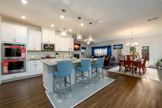 kitchen with light stone countertops, stainless steel appliances, pendant lighting, a kitchen island with sink, and white cabinets