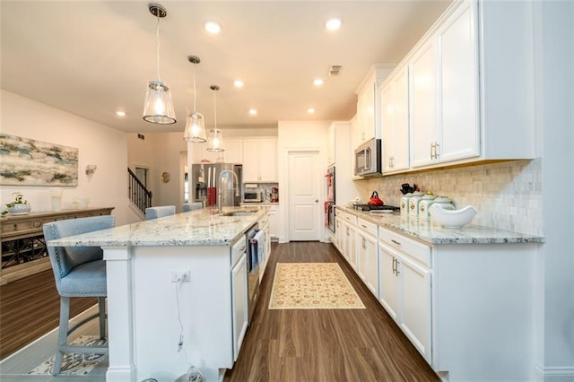 kitchen with white cabinets, backsplash, stainless steel appliances, and a center island with sink