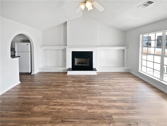 unfurnished living room with ceiling fan, lofted ceiling, dark hardwood / wood-style floors, and a textured ceiling