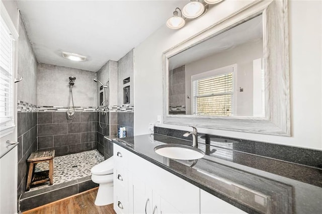 bathroom featuring hardwood / wood-style floors, vanity, a tile shower, and toilet