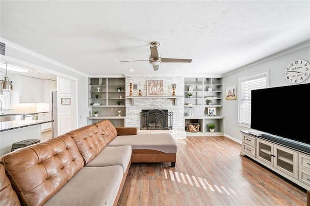 living room with a brick fireplace, ornamental molding, light hardwood / wood-style floors, and ceiling fan