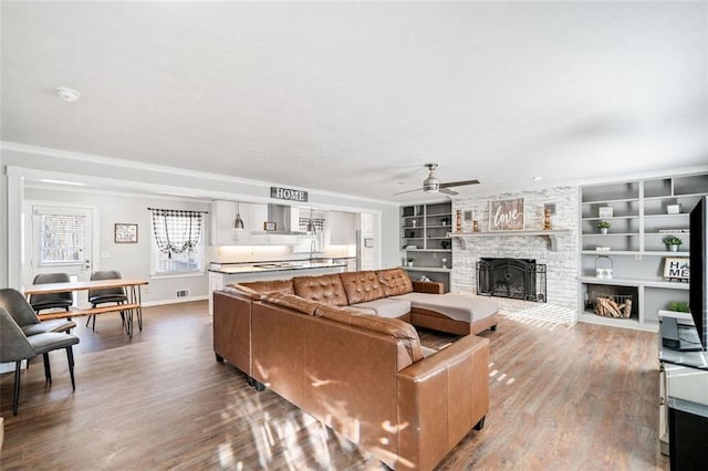 living room with built in shelves, ceiling fan, a fireplace, and hardwood / wood-style floors