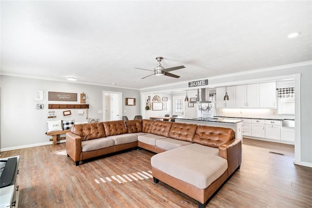 living room featuring ceiling fan, ornamental molding, and light wood-type flooring