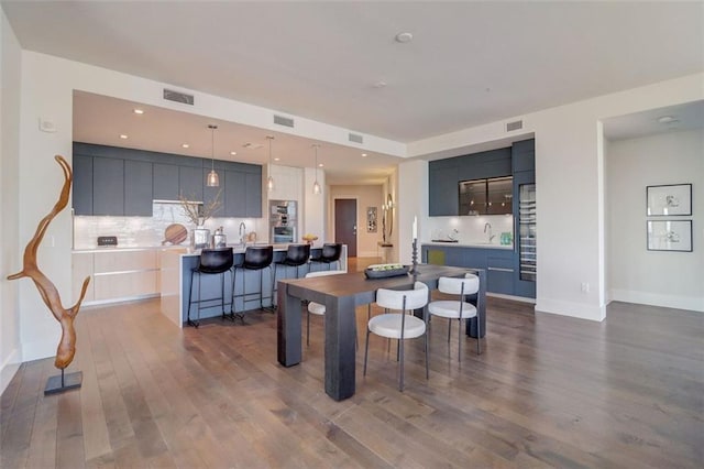 kitchen featuring a center island with sink, decorative light fixtures, dark hardwood / wood-style flooring, decorative backsplash, and a breakfast bar