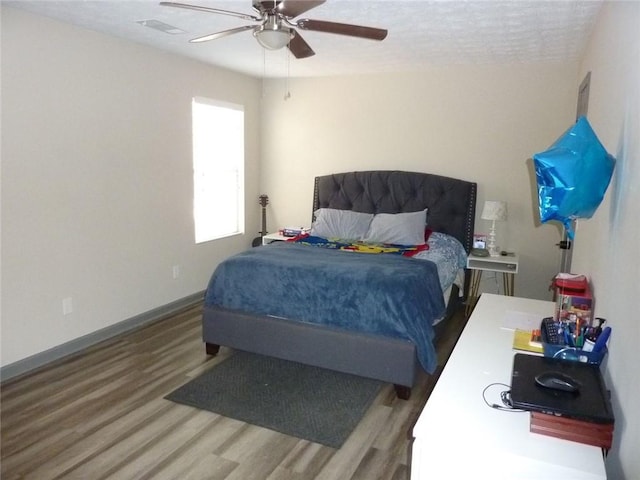 bedroom with a ceiling fan, visible vents, baseboards, and wood finished floors