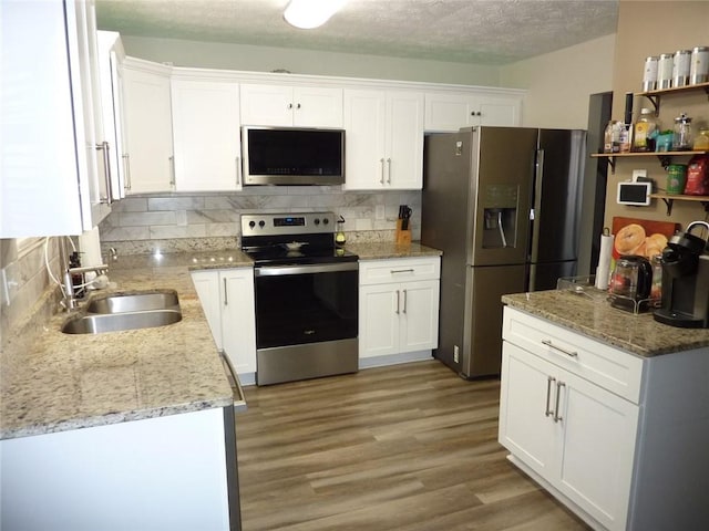 kitchen featuring a sink, white cabinetry, appliances with stainless steel finishes, backsplash, and light wood finished floors