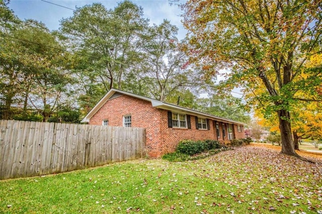 view of side of property featuring a yard, brick siding, and fence