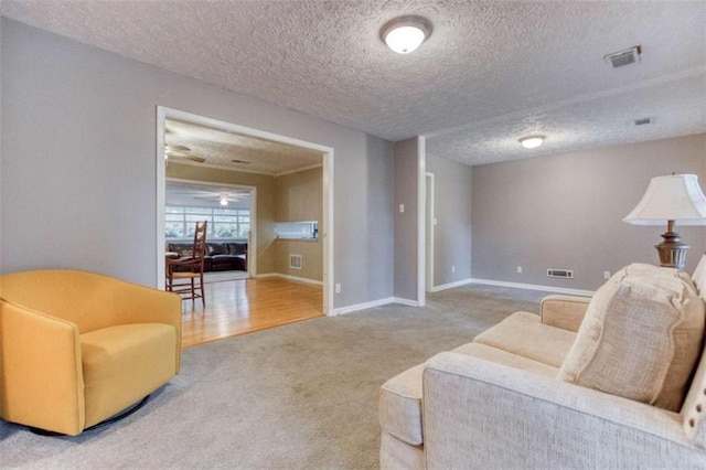 carpeted living area with a ceiling fan, baseboards, visible vents, and a textured ceiling