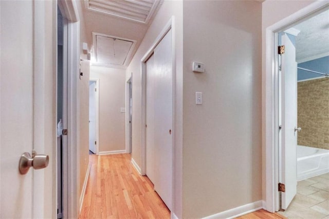 hall featuring light wood-type flooring, attic access, and baseboards