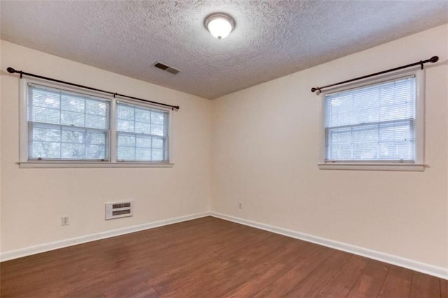 spare room with a wealth of natural light, visible vents, and wood finished floors