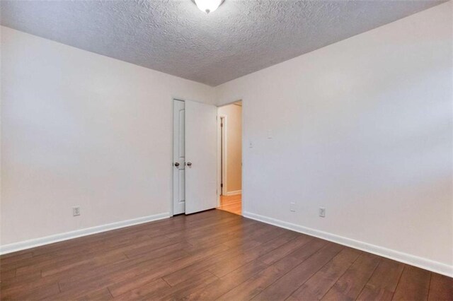 spare room featuring a textured ceiling, dark wood-style flooring, and baseboards