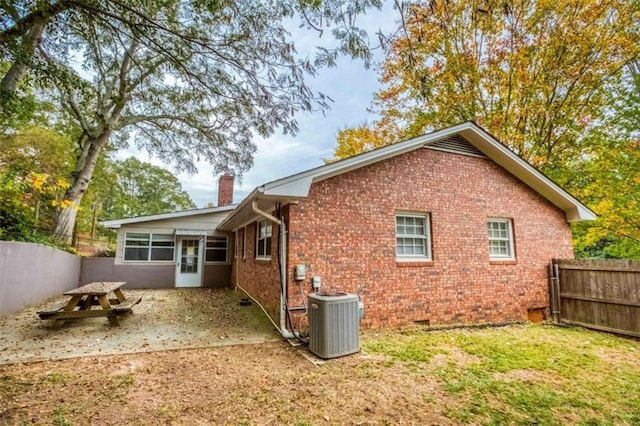 rear view of property with brick siding, a chimney, cooling unit, and fence