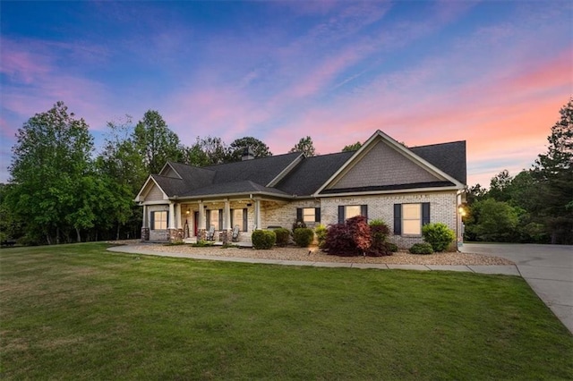 view of front of house featuring covered porch, a yard, and brick siding