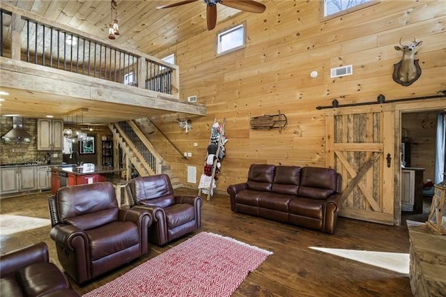 living room with a towering ceiling, ceiling fan, hardwood / wood-style floors, a barn door, and wooden walls