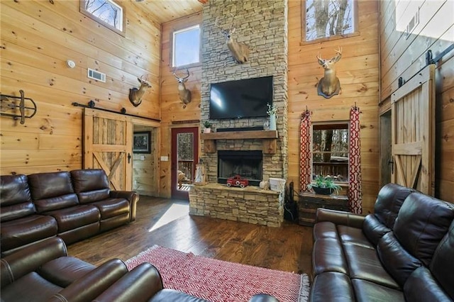 living room featuring a fireplace, hardwood / wood-style floors, wood walls, a barn door, and a towering ceiling