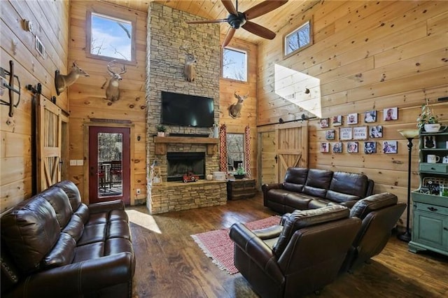 living room featuring hardwood / wood-style flooring, wood walls, a stone fireplace, high vaulted ceiling, and ceiling fan