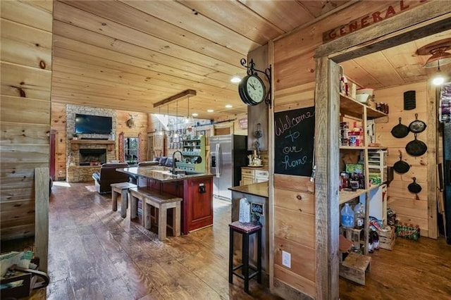 kitchen featuring stainless steel fridge with ice dispenser, dark wood-type flooring, wooden ceiling, wood walls, and a stone fireplace