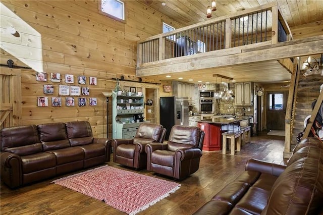 living room featuring dark wood-type flooring, wooden walls, a high ceiling, and a barn door