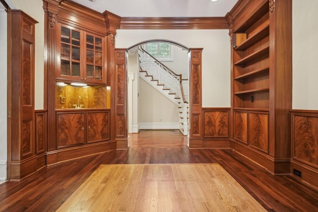 interior space with dark wood finished floors, ornamental molding, stairway, arched walkways, and wainscoting