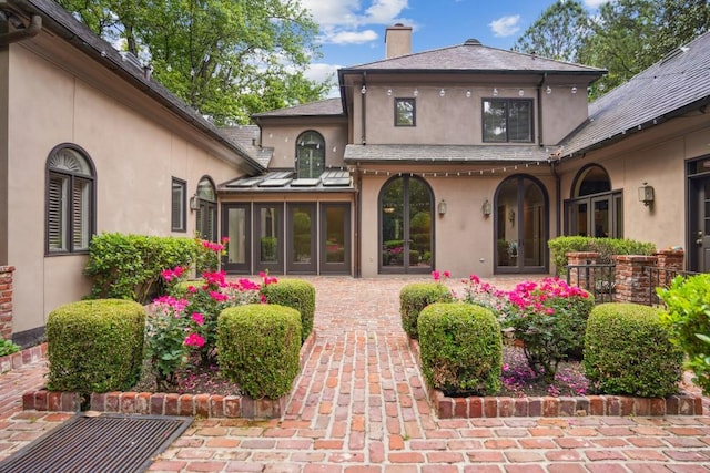rear view of property featuring stucco siding, a chimney, french doors, and a sunroom