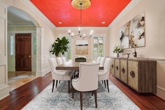 dining space with a decorative wall, arched walkways, wood finished floors, a chandelier, and a wainscoted wall