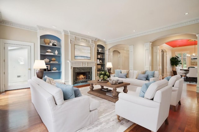 living area with ornamental molding, wood finished floors, arched walkways, built in shelves, and a high end fireplace