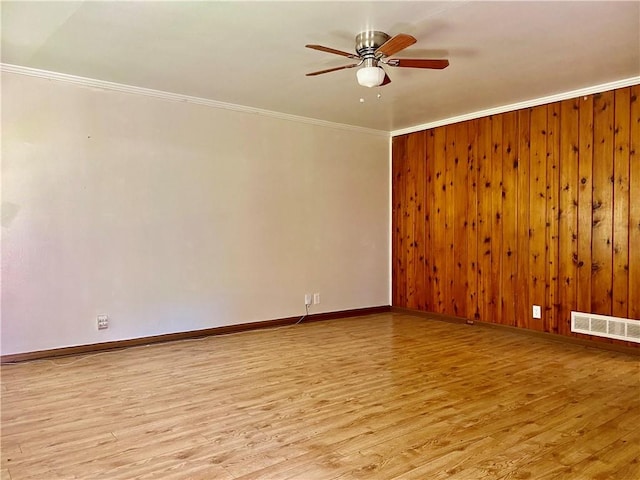 unfurnished room with ceiling fan, light wood-type flooring, wood walls, and crown molding