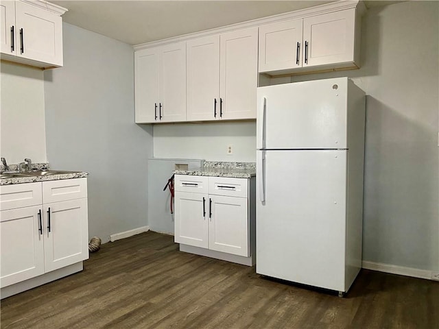 kitchen with white cabinets, white refrigerator, sink, dark wood-type flooring, and light stone countertops