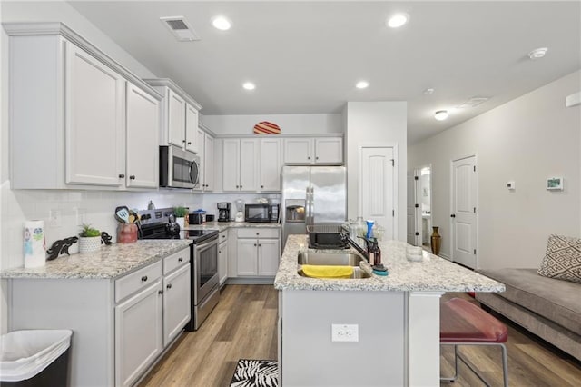 kitchen with appliances with stainless steel finishes, an island with sink, sink, a kitchen breakfast bar, and light hardwood / wood-style flooring