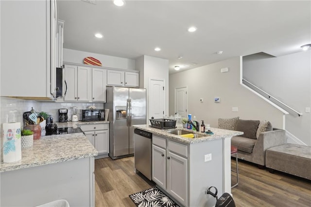 kitchen featuring appliances with stainless steel finishes, backsplash, a kitchen island with sink, light wood-type flooring, and sink