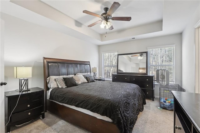 bedroom with light carpet, ceiling fan, a tray ceiling, and multiple windows