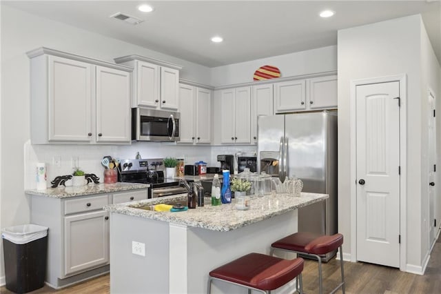 kitchen featuring light stone counters, sink, appliances with stainless steel finishes, and a kitchen island with sink