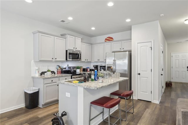 kitchen featuring light stone counters, dark hardwood / wood-style flooring, stainless steel appliances, and an island with sink