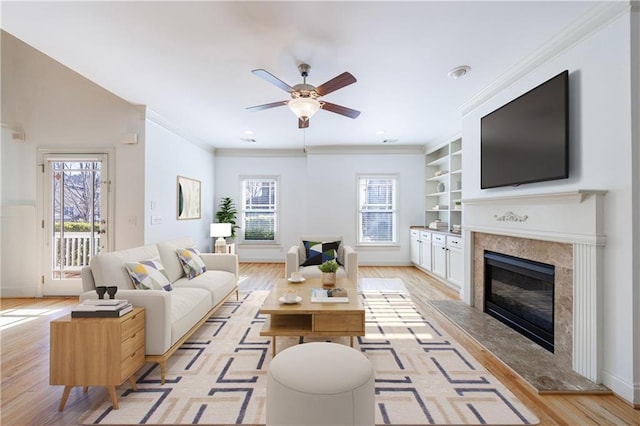 living room featuring light wood-type flooring, built in features, a premium fireplace, and crown molding