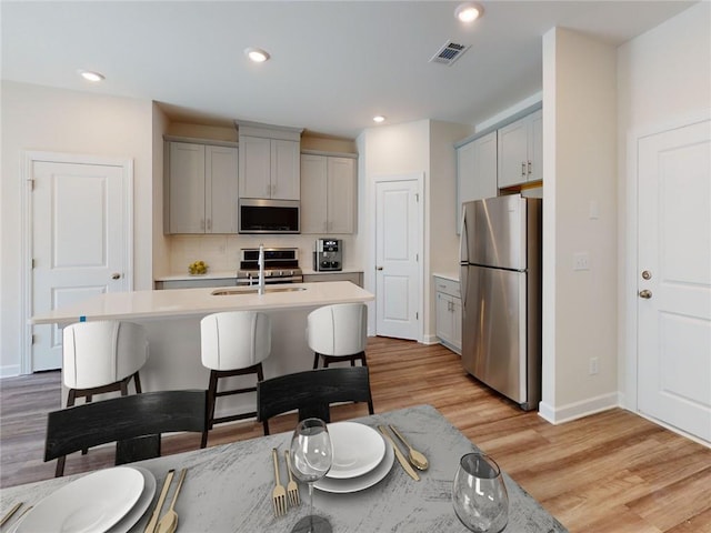 kitchen with sink, appliances with stainless steel finishes, gray cabinets, light hardwood / wood-style floors, and backsplash