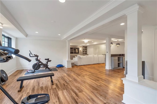 workout area featuring ornate columns, crown molding, a raised ceiling, and light wood-style floors