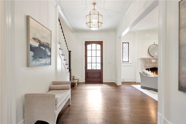 foyer entrance with a chandelier, wood finished floors, a lit fireplace, ornamental molding, and stairway