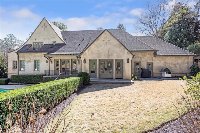 french country style house with french doors, roof with shingles, and stucco siding