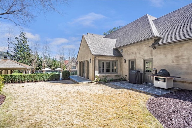 back of house with a patio, a shingled roof, and stucco siding