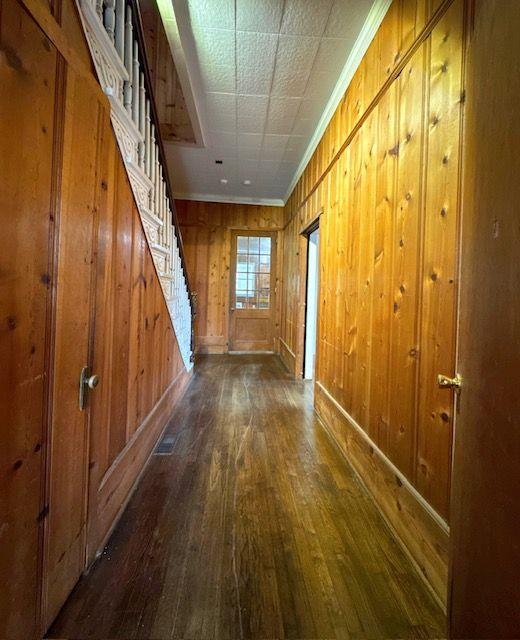 hallway featuring wooden walls, dark hardwood / wood-style floors, and ornamental molding