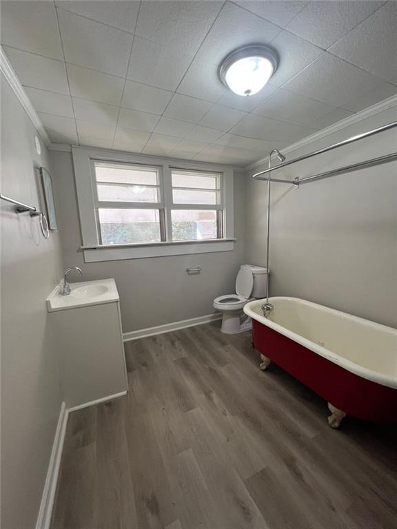 bathroom with a bath, toilet, hardwood / wood-style flooring, vanity, and ornamental molding