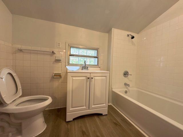 full bathroom featuring tiled shower / bath combo, hardwood / wood-style flooring, vaulted ceiling, and tile walls