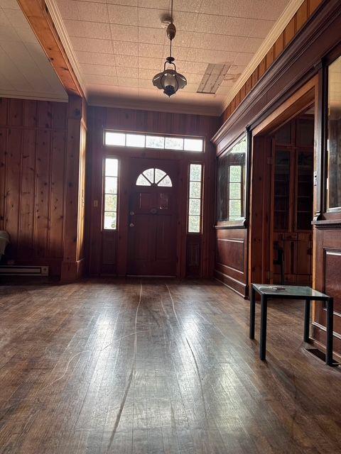 entryway with wooden walls, dark wood-type flooring, and ornamental molding