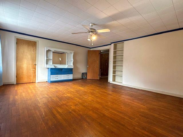 unfurnished living room with crown molding, ceiling fan, built in features, and wood-type flooring